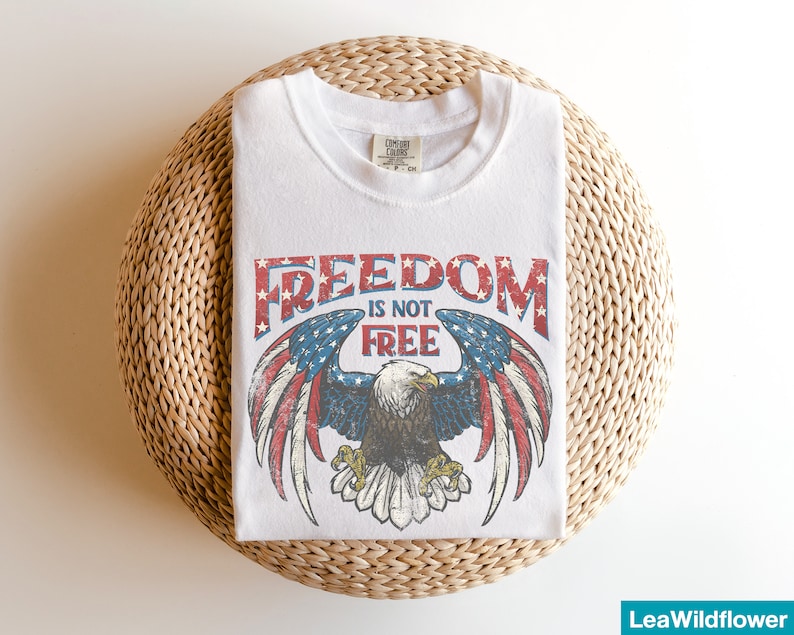 May include: White t-shirt with a vintage-style graphic of an eagle with outstretched wings and the text "FREEDOM IS NOT FREE".