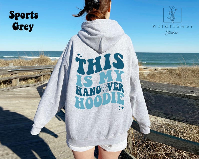 May include: A gray hooded sweatshirt with the text "This is my hangover hoodie" in blue and teal lettering. The text is in a retro font with a smiley face graphic.