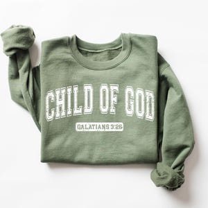 May include: A green sweatshirt with the text "CHILD OF GOD" in white lettering and "GALATIANS 3:26" in smaller white lettering below.