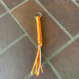 May include: A keychain made of orange, yellow, and white braided string with a silver metal ring at the top.