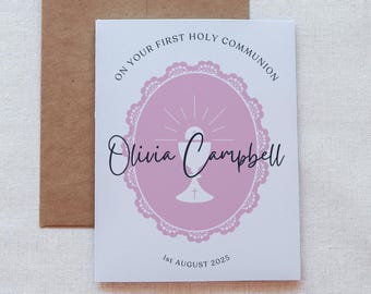 May include: White card with pink and black text and a pink and white graphic of a chalice with a host. The text reads "On your first Holy Communion Olivia Campbell 1st August 2025".