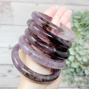 May include: A stack of five amethyst bangles, each with a different shade of purple and black. The bangles are smooth and polished, and they have a natural, organic look.