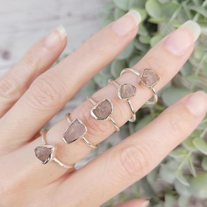 May include: Five silver rings with raw rose quartz stones. Each ring features a different sized stone, showcasing the natural beauty of the crystal.
