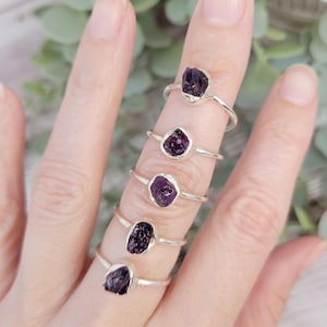 May include: Five silver rings with raw amethyst stones. Each ring features a different size and shape of amethyst, showcasing the natural beauty of the gemstone.
