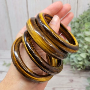 May include: Four stacked tiger's eye stone bangles. The bangles are a rich golden brown color with dark brown stripes. The bangles are polished and have a smooth, glossy finish.