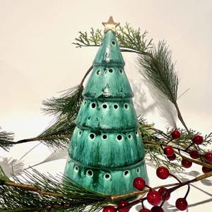 May include: A conical ceramic Christmas tree sculpture in shades of teal and dark green with a glossy finish. The tree features multiple rows of small circular cutouts and is topped with a single, small, light-colored star ornament.
