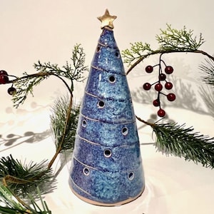 May include: A conical ceramic sculpture in shades of blue with a speckled glaze finish. The object features a spiral pattern of small circular cutouts and is topped with a gold-colored star. The surface has a glossy, textured appearance.