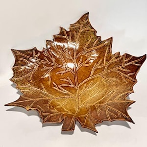 May include: A ceramic leaf-shaped dish with a brown and gold glaze. The dish is detailed with raised lines that resemble the veins of a leaf.