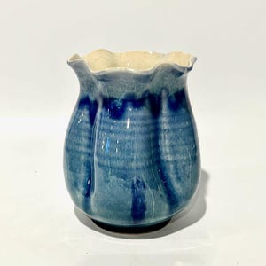 May include: A handmade ceramic vase with a unique, ruffled rim. The vase features a blue glaze with darker blue streaks, creating a textured appearance. The interior rim is a light beige color. This decorative vase is suitable for displaying flowers or as a standalone art piece.