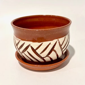 May include: A terracotta planter with a white geometric design. The planter has a matching saucer.