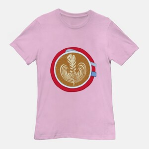 Op de afbeelding: Een roze t-shirt met een rode cirkel met daarin een latte met een bladerenontwerp.