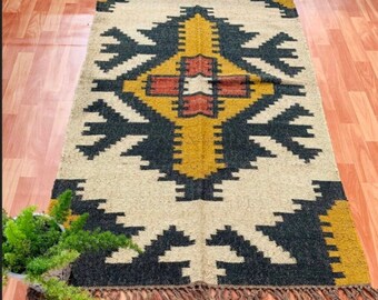 May include: A hand-woven rug with a geometric pattern in black, white, yellow, and red. The rug has a fringe border.
