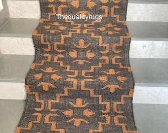May include: A brown and orange geometric patterned runner rug is placed on a set of stairs. The rug has a repeating pattern of squares and stylized flowers. The text "Thequalityrugs" is visible on the rug.