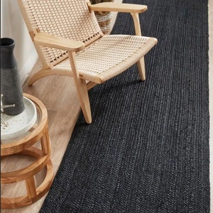 May include: A black jute rug runner with a woven texture. The rug is placed on a wooden floor and a light wood chair is positioned on top of the rug.