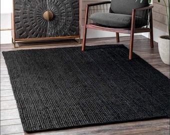 May include: Black jute rug with a woven texture. The rug is placed in a living room setting with a wooden chair and a cabinet with a decorative door.