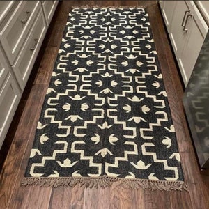 May include: Black and white geometric patterned rug with fringe on the edges. The rug is made of natural fibers and has a rustic look.