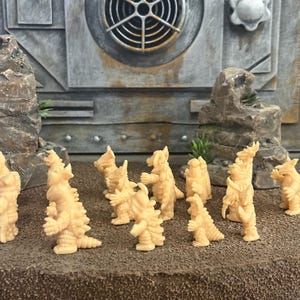Peut inclure: Une collection de onze petites figurines de monstres en plastique beige clair non peintes. Chaque cr&eacute;ature pr&eacute;sente une posture bip&egrave;de, une peau textur&eacute;e avec des pointes et des traits distincts. Les figurines sont dispos&eacute;es en groupe sur une surface textur&eacute;e.