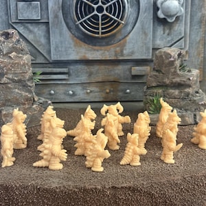Peut inclure: Une collection de petites figurines de monstres en plastique beige clair non peintes, dispos&eacute;es en groupe. Chaque figurine pr&eacute;sente des &eacute;cailles reptiliennes, des pointes et des cornes distinctes, avec des postures bip&egrave;des et des traits uniques.