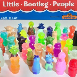 May include: A collection of colorful, translucent Little Bootleg People figures. The figures are in various colors, including green, pink, blue, and orange. The packaging reads "Little Bootleg People" and "AGES: 20 & UP".