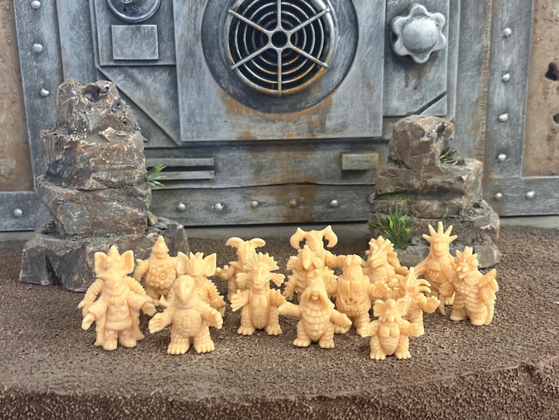 Peut inclure: Une collection de quinze petites figurines de monstres beiges et monochromes pr&eacute;sentant divers designs de cr&eacute;atures avec des cornes, des &eacute;cailles et des pointes, dispos&eacute;es en groupe devant deux formations rocheuses et un panneau mural industriel.