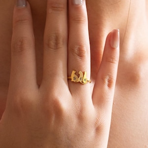 Op de afbeelding: Een gouden ring met de letters "SEB" gespeld in een uniek lettertype. De ring wordt gedragen aan de ringvinger van een hand.