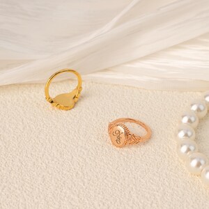 May include: Two gold rings on a white background. The ring on the left has a heart-shaped design. The ring on the right has an oval-shaped design with the word "Hope" engraved on it.