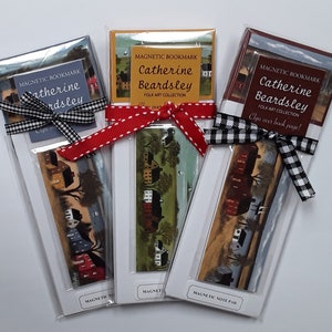 May include: Three magnetic bookmarks featuring artwork by Catherine Beardsley. Each bookmark has a different scene of houses and trees. The bookmarks are packaged in clear plastic with a ribbon tied around them. The text on the bookmarks reads "Magnetic Bookmark" and "Catherine Beardsley Folk Art Collection".