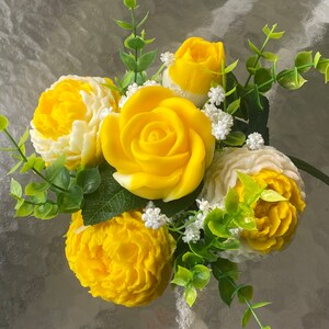 May include: A bouquet of yellow and white soap flowers with green leaves. The flowers are arranged in a circular shape and are made to look like roses and carnations.