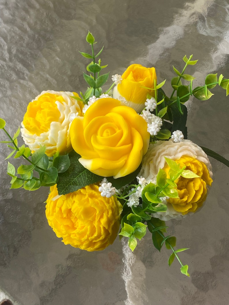 May include: A bouquet of yellow and white soap flowers with green leaves. The flowers are arranged in a circular shape and are made to look like roses and carnations.