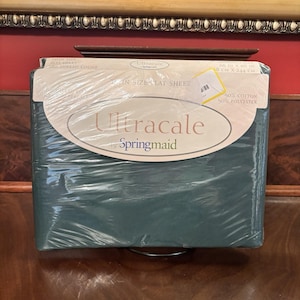 Puede incluir: Una sábana plana individual empaquetada en color verde oscuro. El embalaje muestra el logotipo "Ultracale by Springmaid" e información del producto, incluido el número de hilos y las dimensiones de 168 cm x 244 cm.