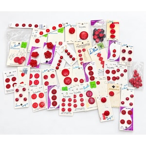 May include: A large collection of red buttons in various shapes and sizes, including round, flower-shaped, and textured designs. Many buttons are attached to branded cardboard display cards labeled Le Bouton, La Mode, and Streamline, while others are in plastic bags.