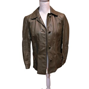 May include: Olive green leather jacket with a classic collar, three buttons, and two front pockets. The jacket is displayed on a white mannequin. The leather has a slightly worn appearance.