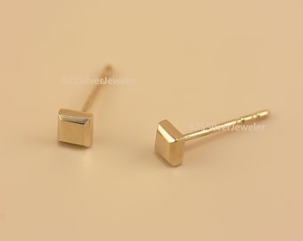 May include: A pair of gold square stud earrings. The earrings are small and simple, with a minimalist design.