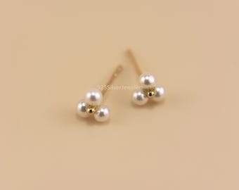 May include: A pair of gold stud earrings with three small white pearls each.