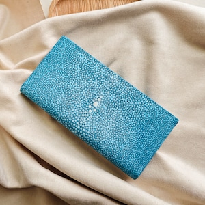 May include: A blue leather wallet with a textured, patterned surface. The wallet is made of stingray skin.