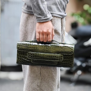 Può includere: Una pochette in pelle di coccodrillo verde con chiusura a lembo e manico superiore.