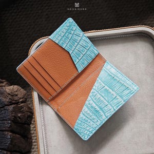 May include: Open leather wallet with a turquoise crocodile-textured accent and brown interior. The wallet has multiple card slots and is displayed open. The brand name "MESSIEURS" is printed at the top.