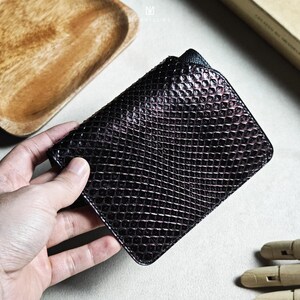 May include: A dark brown wallet with a textured, scale-like pattern. The wallet is rectangular and appears to be made of leather. The image is taken from a slightly elevated angle, showcasing the wallet's design and texture.