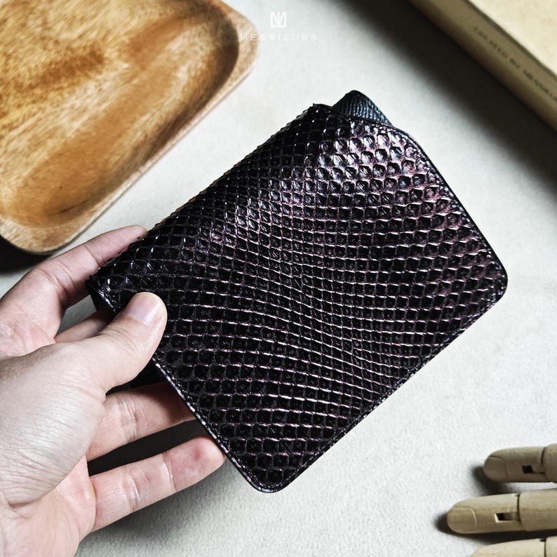 May include: A dark brown wallet with a textured, scale-like pattern. The wallet is rectangular and appears to be made of leather. The image is taken from a slightly elevated angle, showcasing the wallet's design and texture.