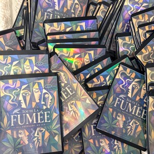 May include: A collection of rectangular holographic pouches featuring a cubist-style illustration of faces, cannabis leaves, and the text "TOUTE LA FUM&Eacute;E" and "ALL PRESSURE, NO AIR" printed in a bold, dark font against a colorful, geometric background.