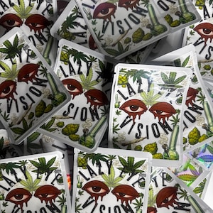 May include: A collection of rectangular white pouches featuring a graphic print of two bloodshot eyes with red drips, green cannabis leaves, a smoking green glass bong, and a rolled cigarette. The text LAZY EYE VISION is printed in black.