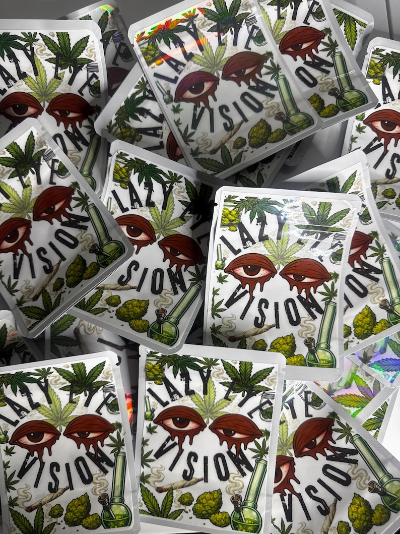 May include: A collection of rectangular white pouches featuring a graphic print of two bloodshot eyes with red drips, green cannabis leaves, a smoking green glass bong, and a rolled cigarette. The text LAZY EYE VISION is printed in black.