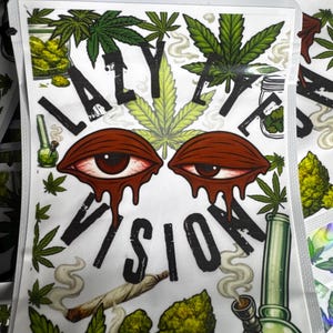 May include: A rectangular white pouch featuring the text LAZY EYE VISION in black letters. The design includes two red, bloodshot, melting eyes, green cannabis leaves, a lit joint, and a green glass water pipe with swirling smoke.