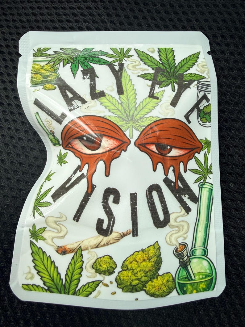 May include: A white resealable pouch featuring the text LAZY EYE VISION in black letters. The design includes two red, bloodshot eyes with dripping effects, green cannabis leaves, a lit joint, and a green glass water pipe with smoke.