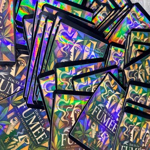 May include: A collection of rectangular holographic product pouches featuring a geometric illustration of faces and cannabis leaves. The text on each pouch reads TOUTE LA FUMEE, ALL PRESSURE, NO AIR, and includes the initials TF at the bottom.