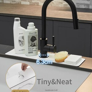May include: White sink organizer with a black faucet and two bottles of cleaning supplies. The organizer has a 6.3 inch wide space for the faucet. The text "Tiny & Neat Handmade Craft" is printed on the organizer.