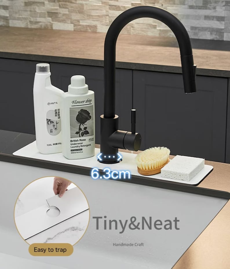 May include: White sink organizer with a black faucet and two bottles of cleaning supplies. The organizer has a 6.3 inch wide space for the faucet. The text "Tiny & Neat Handmade Craft" is printed on the organizer.