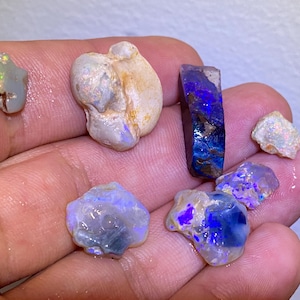 May include: A collection of raw opals in various shapes and sizes. The opals display a range of colors, including blue, purple, white, and hints of green. Some opals have a rough, natural texture, while others have a more polished appearance.