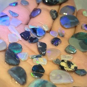 May include: A collection of iridescent opal gemstones in various shades of blue, green, and white. The opals are rough and have a natural, irregular shape.