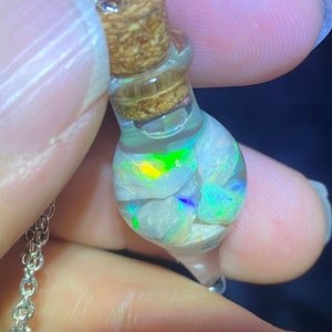 May include: A glass vial pendant necklace with a silver chain. The vial is filled with iridescent opal stones and a cork stopper.